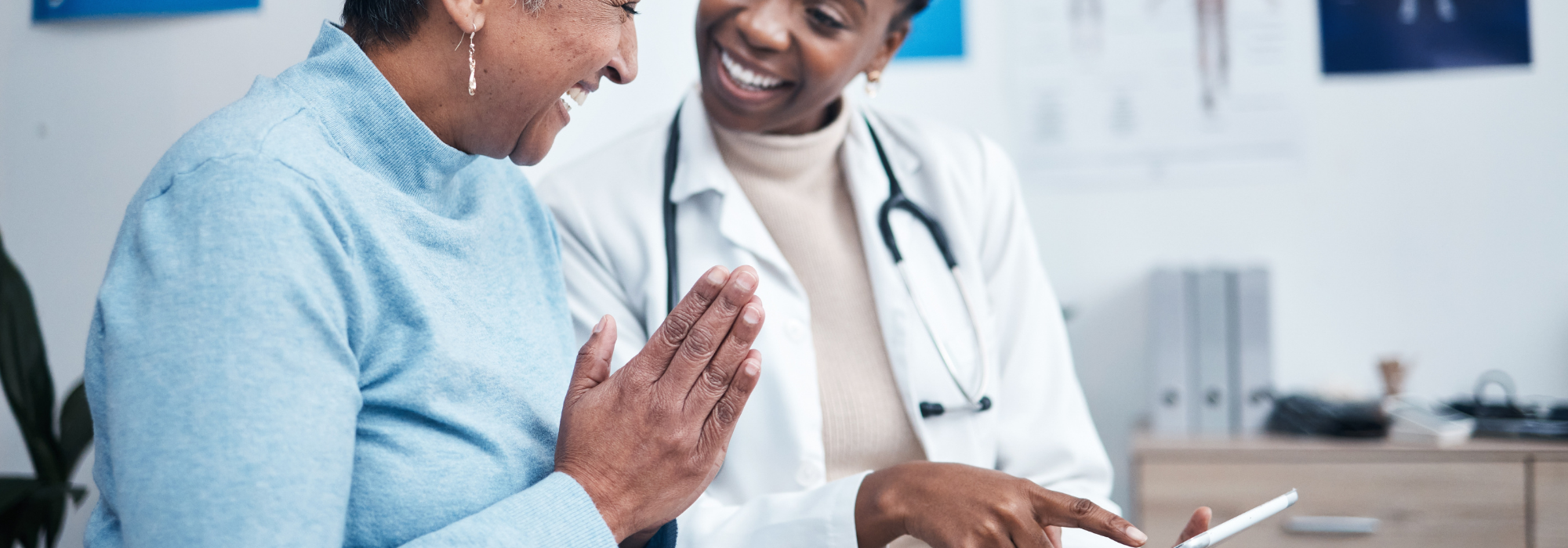 A smiling patient consults with a female doctor in a medical office, reviewing health information on a digital tablet, symbolizing patient-centered care, preventive healthcare, and cloud security for healthcare providers.
