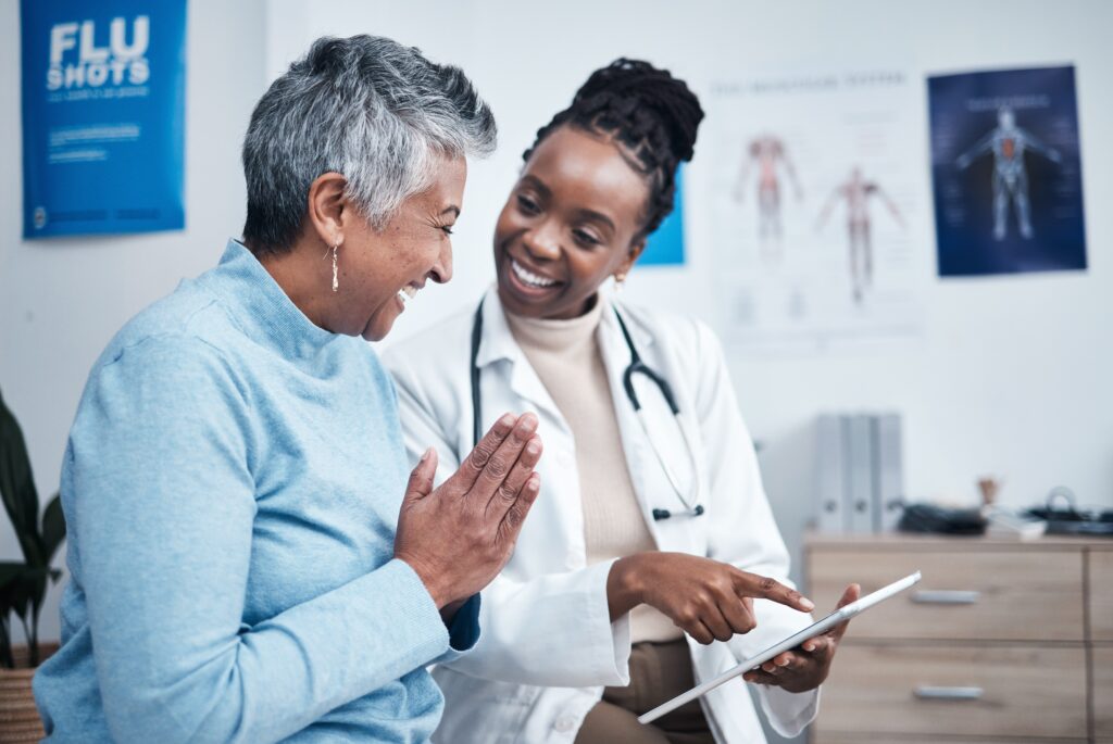 A smiling patient consults with a female doctor in a medical office, reviewing health information on a digital tablet, symbolizing patient-centered care, preventive healthcare, and cloud security for healthcare providers.